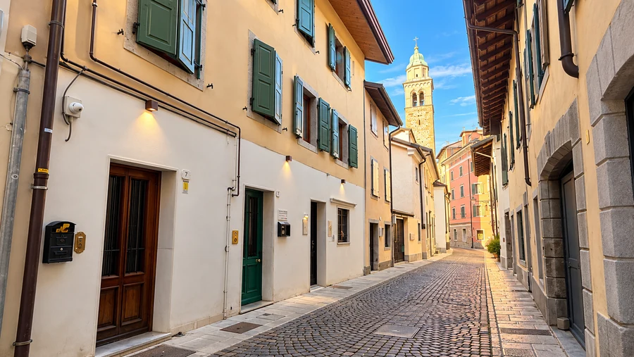 Vicolo lastricato del centro storico di Udine con case dalle persiane verdi e un campanile sullo sfondo