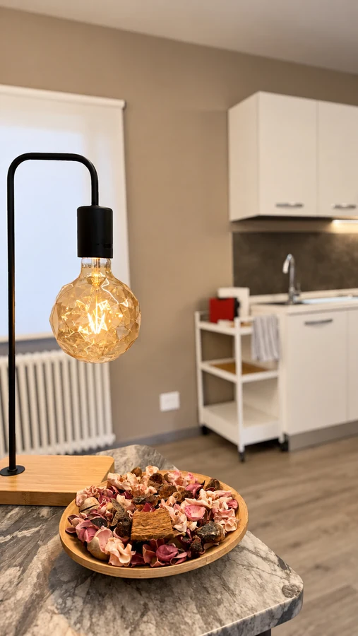 Lampada a filamento e vassoio sul ripiano in pietra, con la cucina di Alkecè Red sullo sfondo
